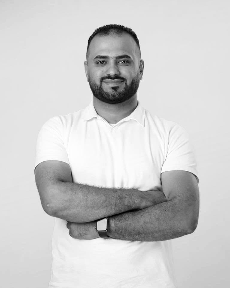 Salah Moustafa, in a white shirt with his arms crossed, photographed against a plain studio backdrop.